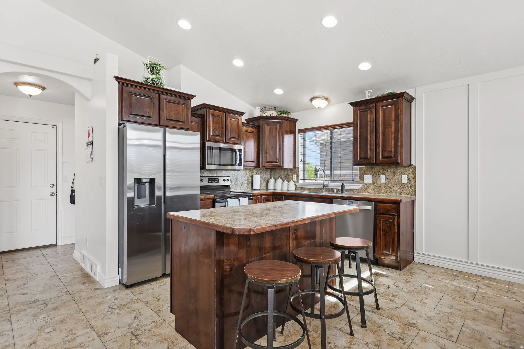 Kitchen featuring a breakfast bar island, wood-finish cabinetry, stainless steel appliances, tile flooring, and recessed lighting