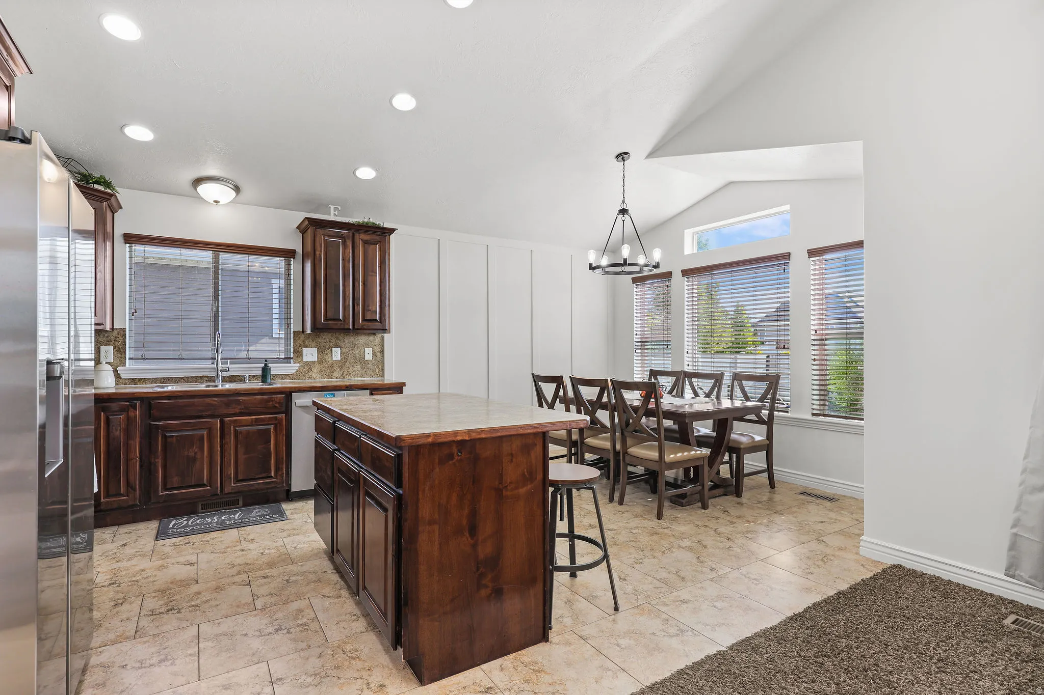 Kitchen and dining area featuring a central island with a stone-finish countertop, recessed lighting, and rich wood cabinetry