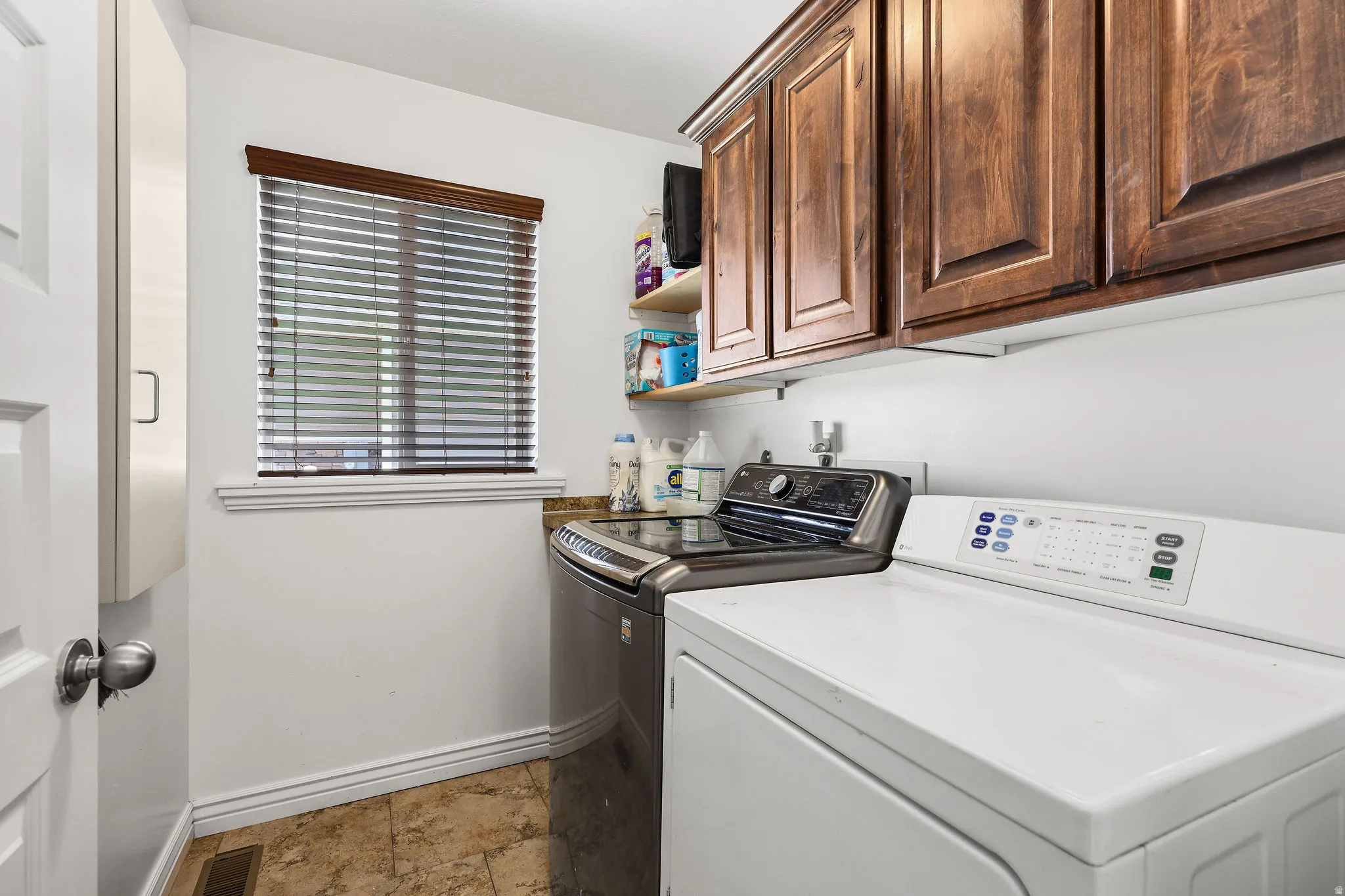 Dedicated laundry space featuring a window with blinds, wood-finish upper cabinetry, a utility countertop, and tile flooring