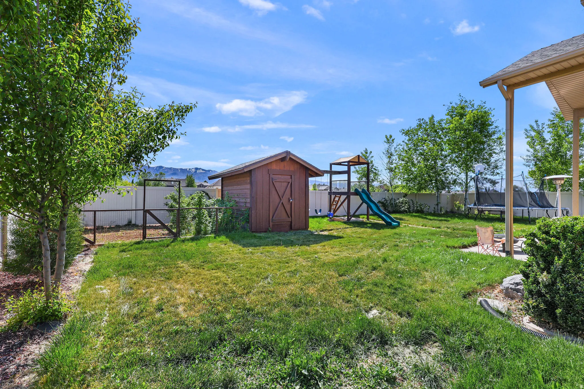 Expansive backyard featuring a manicured lawn, a wooden storage shed, a vinyl privacy fence, a covered patio area, and mature trees