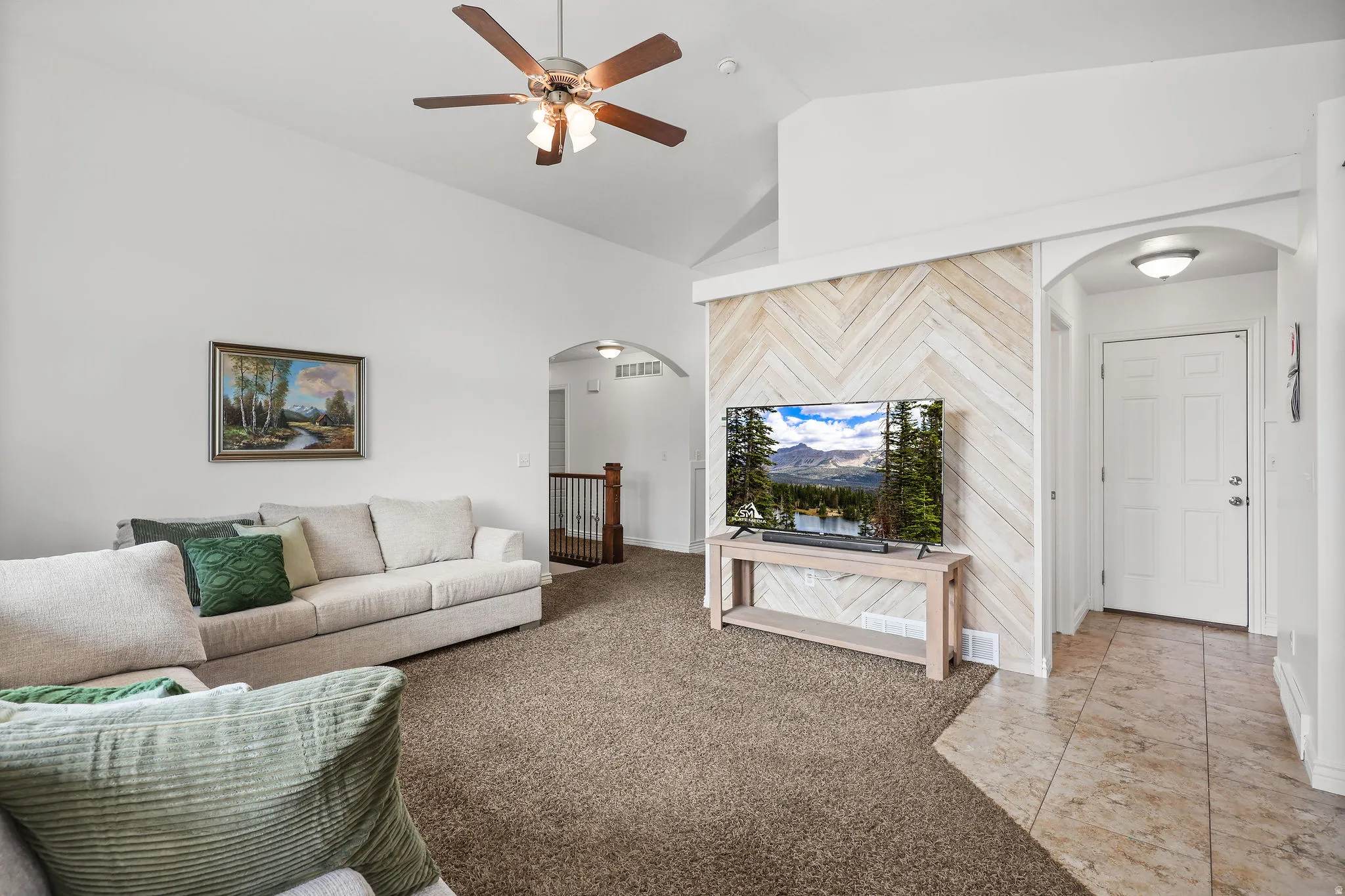 Vaulted ceiling living area featuring a ceiling fan with integrated lighting, a decorative chevron wood-finish accent wall, and a tiled entryway
