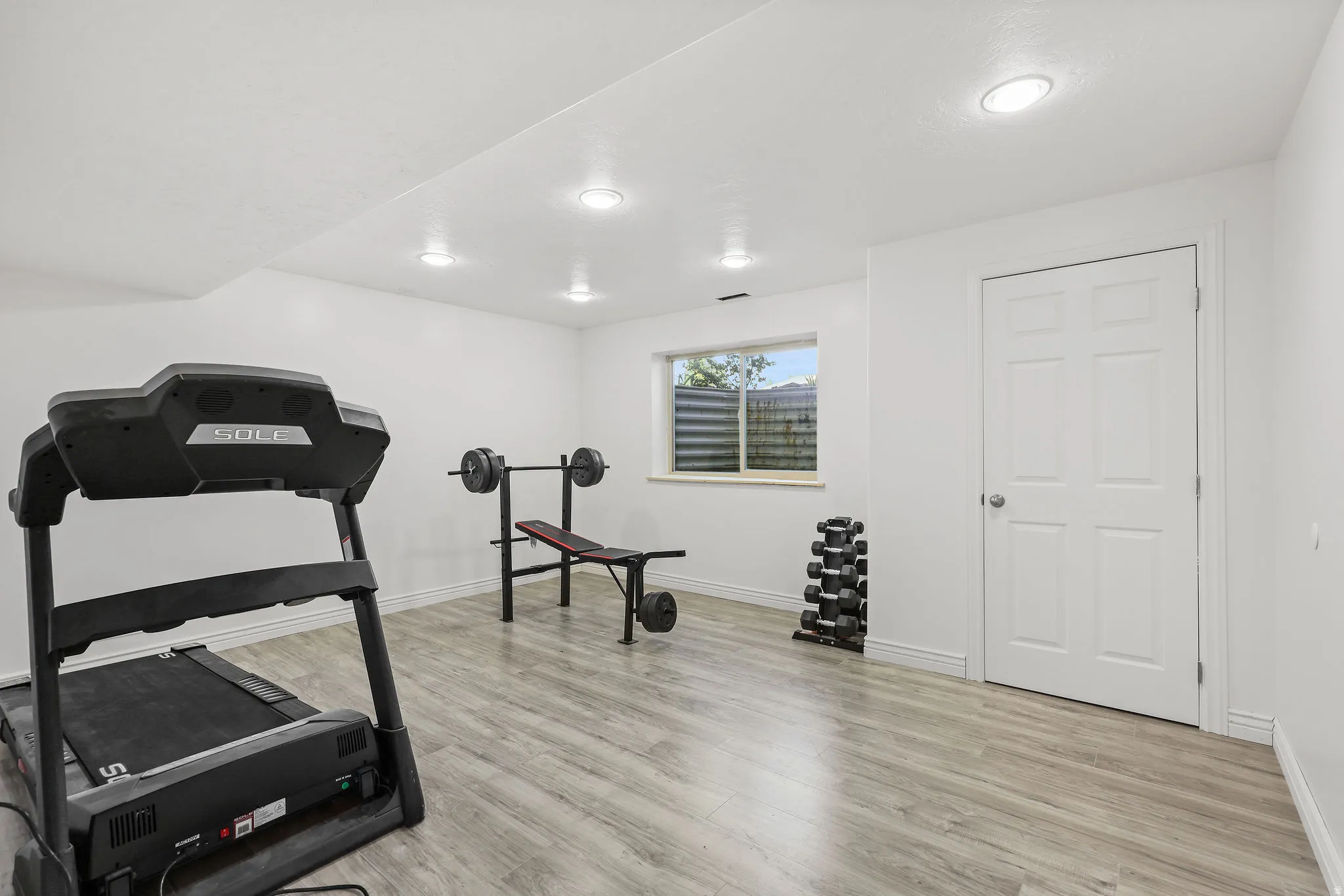 Spacious room featuring light wood-finish flooring, recessed lighting, and a white six-panel door