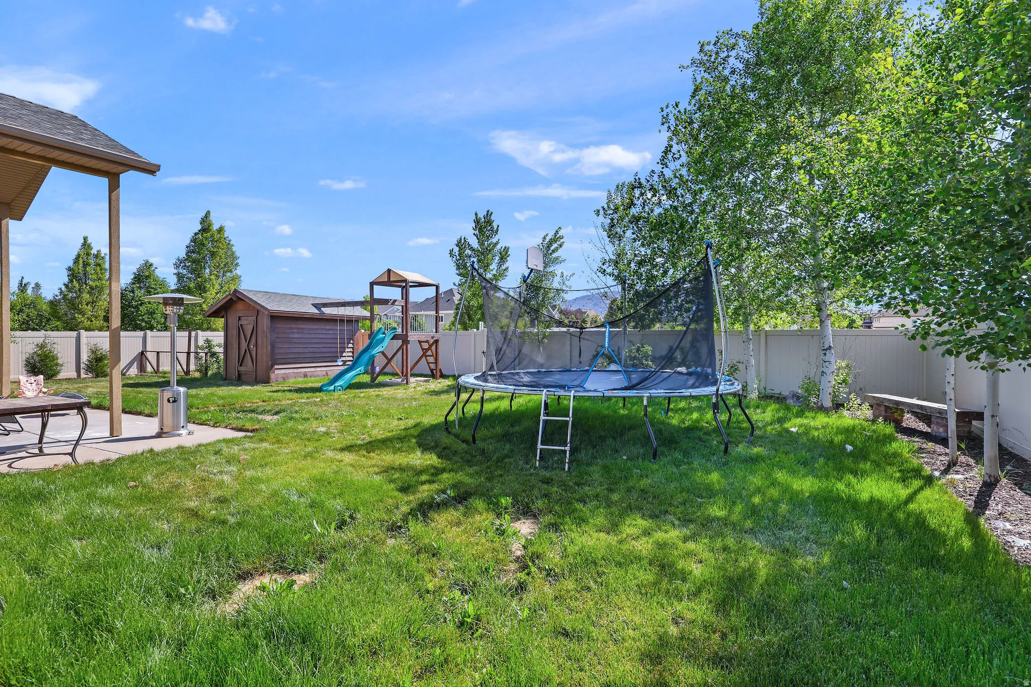 Expansive backyard featuring a covered patio, manicured lawn, and mature trees