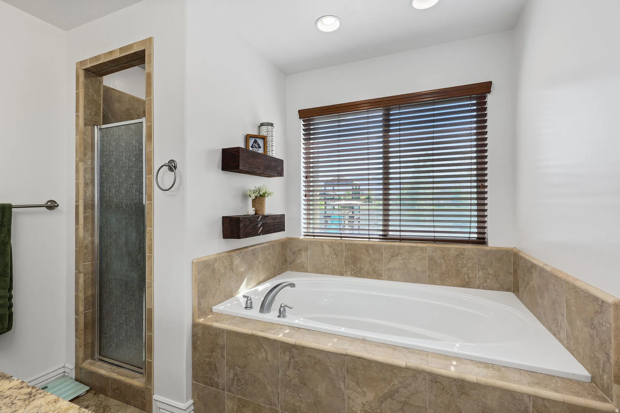 White drop-in tub with a tile surround, accompanied by a separate shower enclosure with a glass door