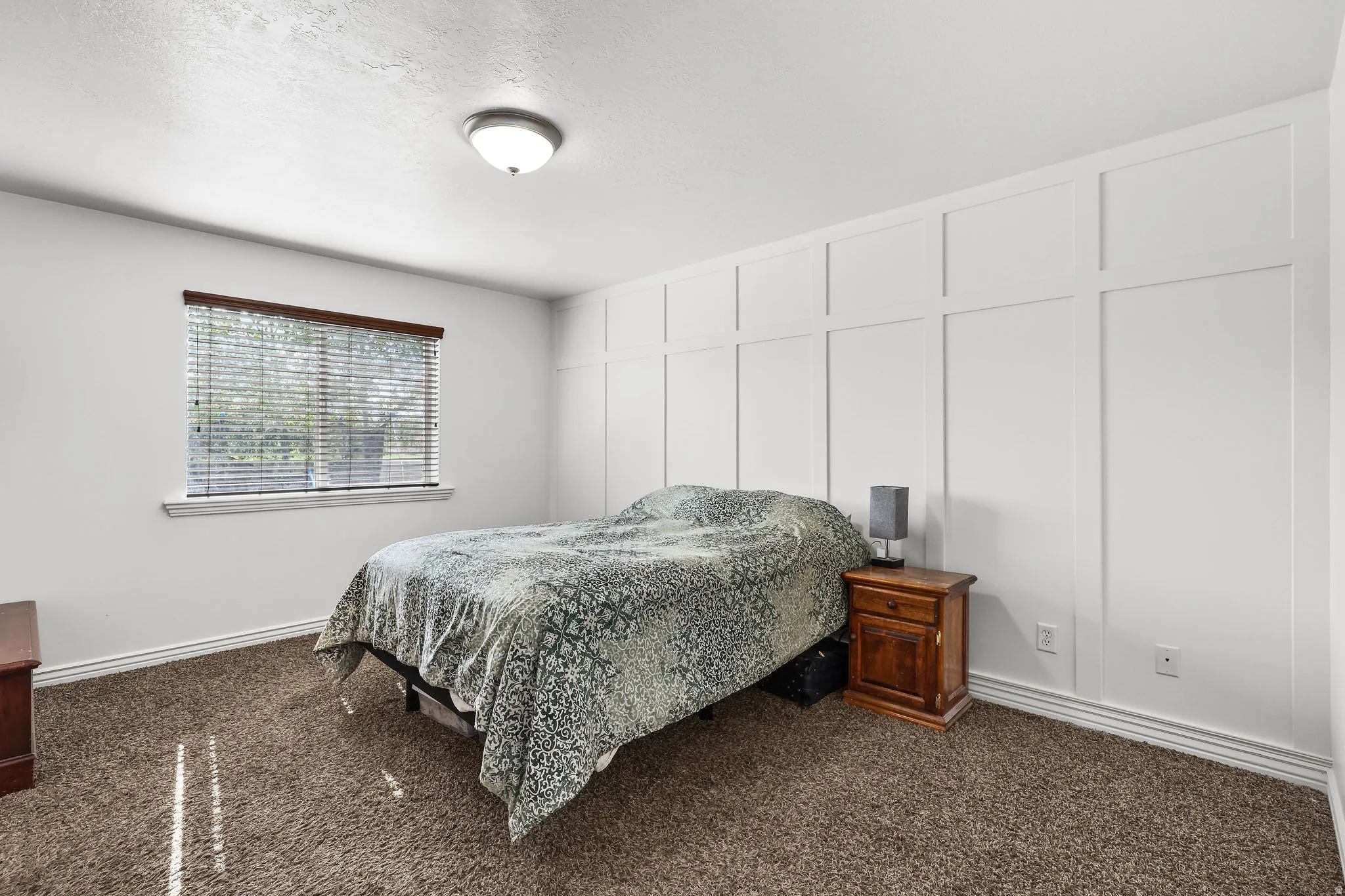 Bedroom featuring a decorative board and batten accent wall, neutral tone carpet, and a flush mount ceiling light fixture