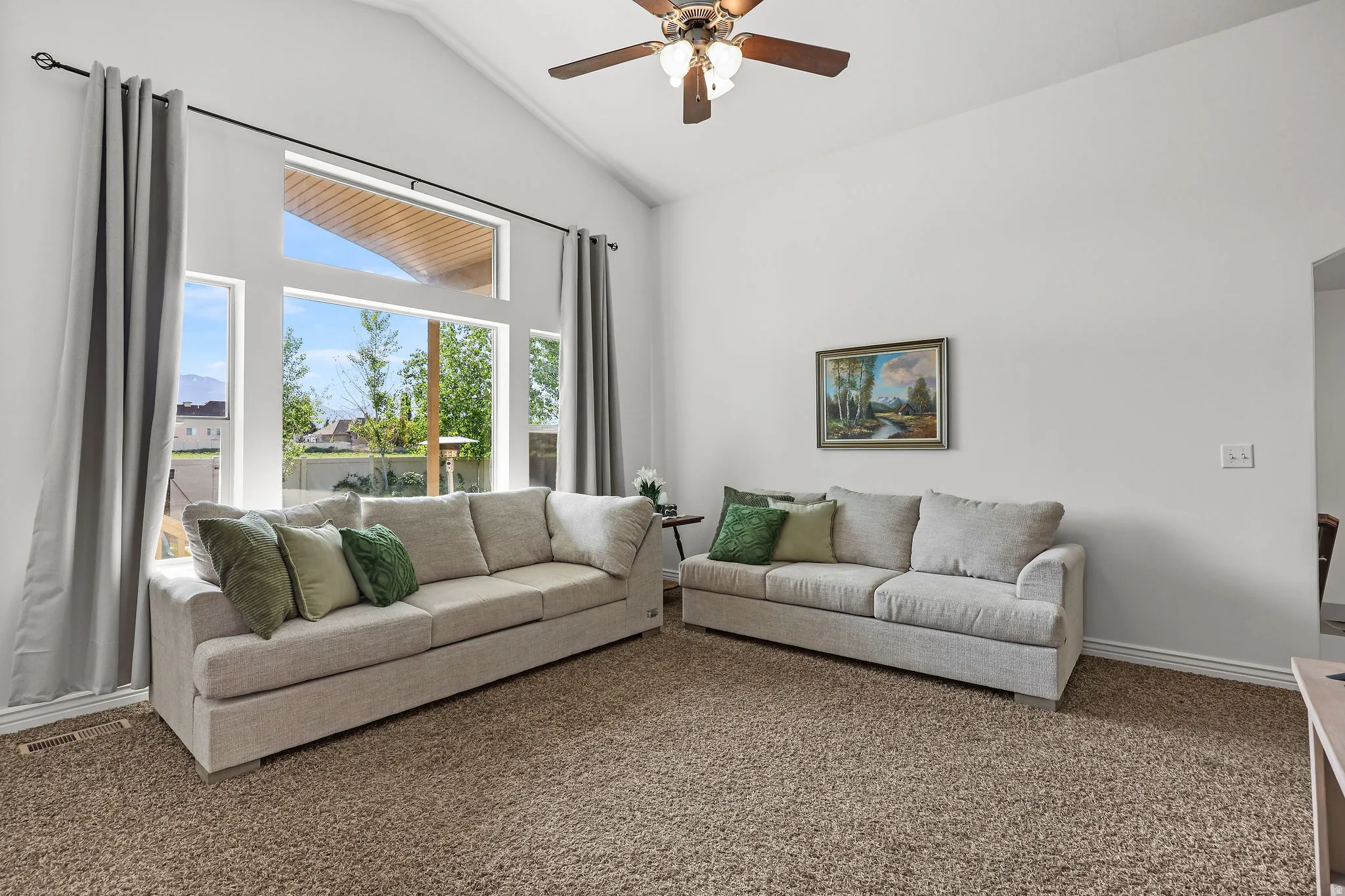 Vaulted ceiling living area featuring a multi-pane window design, a ceiling fan with integrated lighting, and neutral carpet flooring