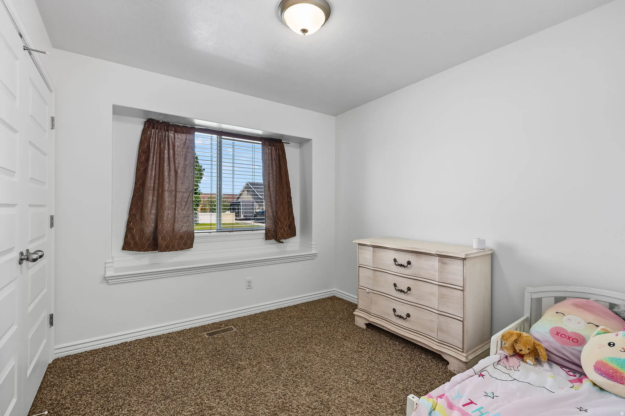 Room featuring neutral-toned walls, a single window with blinds and drapes, and an overhead flush-mount light fixture