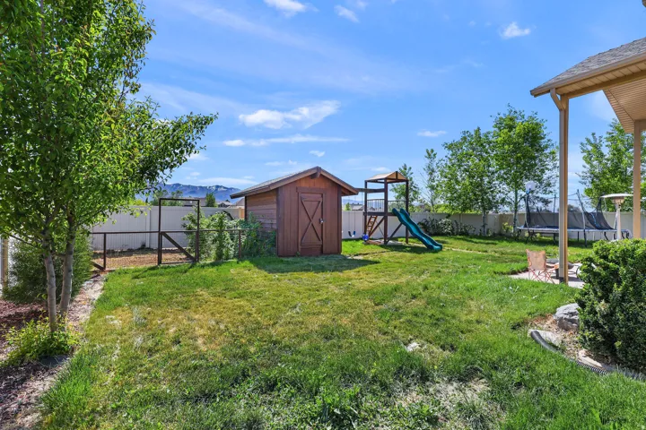 Expansive backyard featuring a manicured lawn, a wooden storage shed, a vinyl privacy fence, a covered patio area, and mature trees