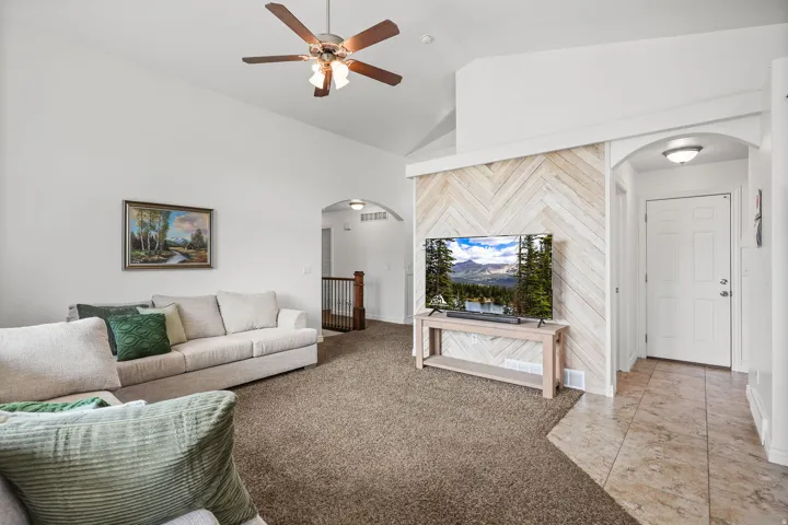 Vaulted ceiling living area featuring a ceiling fan with integrated lighting, a decorative chevron wood-finish accent wall, and a tiled entryway