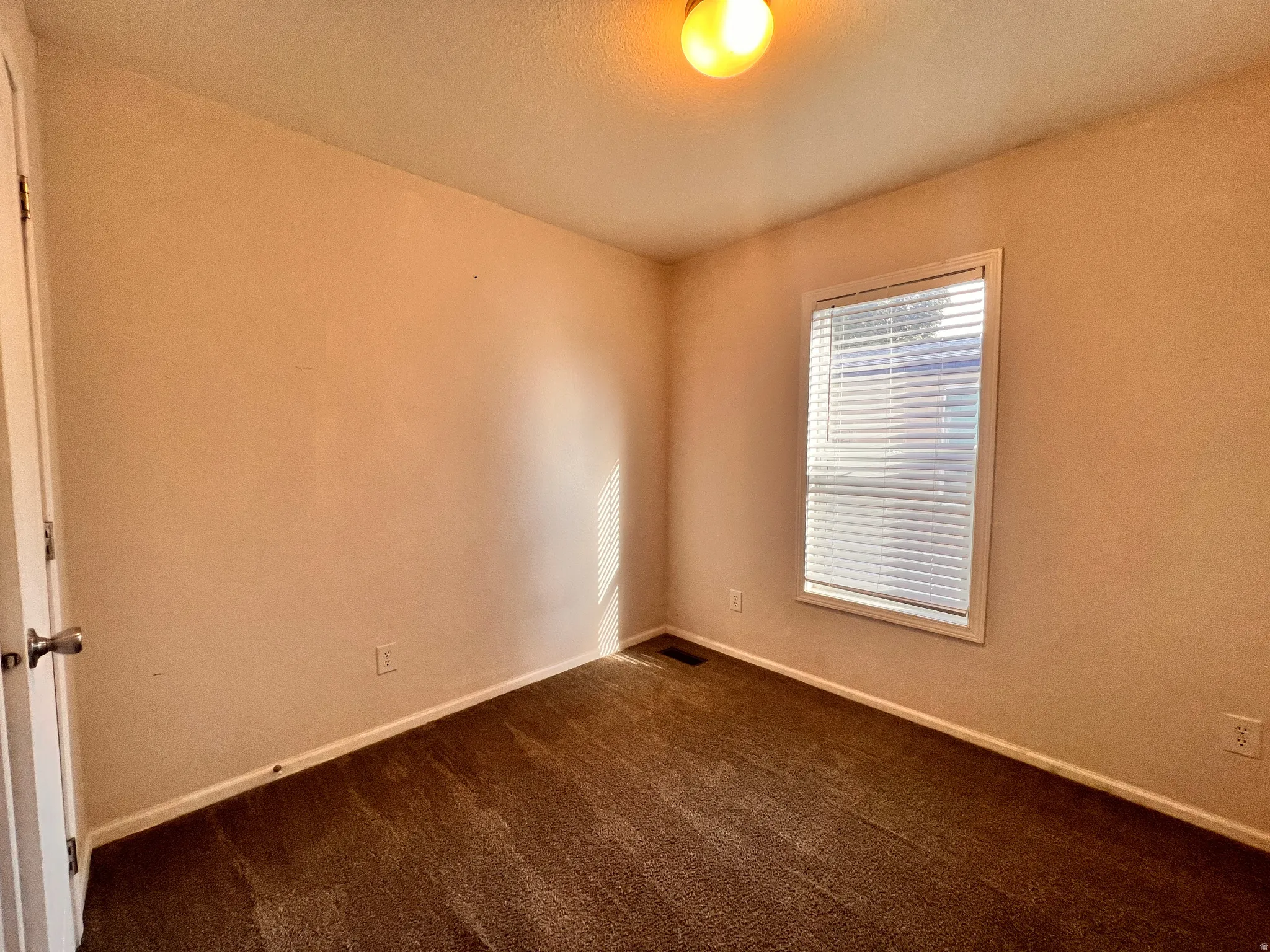 Bedroom featuring neutral-toned walls, brown carpet flooring, and a window with horizontal blinds