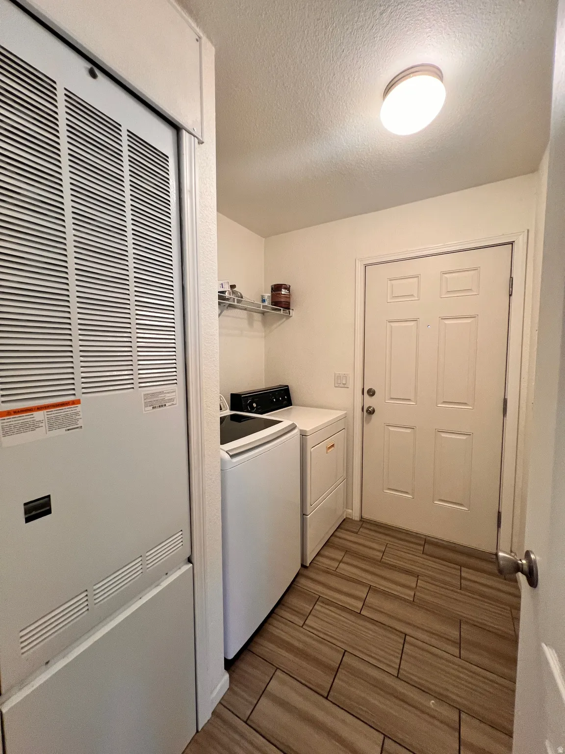Dedicated laundry area featuring wood-finish tile flooring, a paneled entry door, and wall-mounted shelving