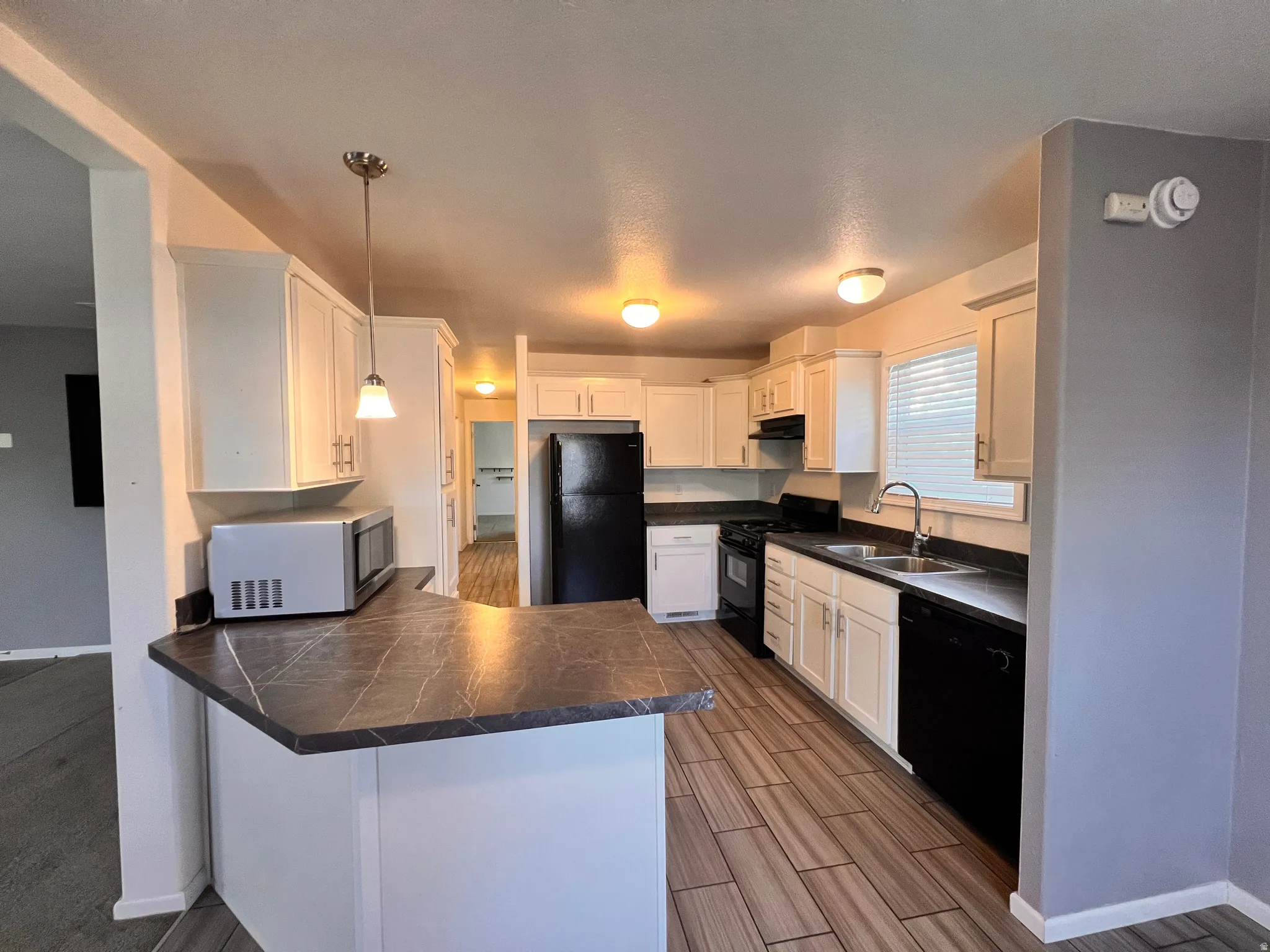 Modern kitchen featuring white cabinetry, dark countertops, wood-finish tile flooring, and integrated black appliances