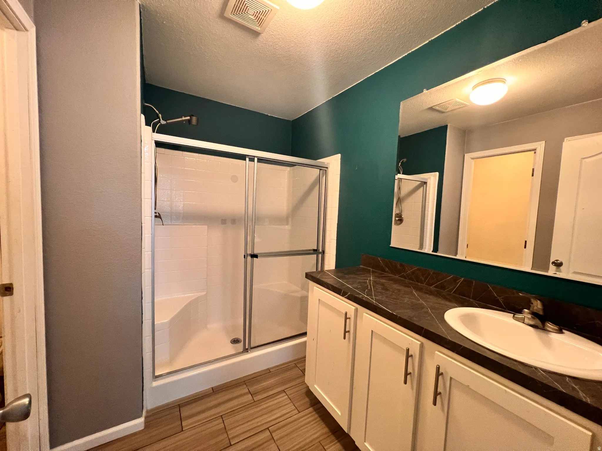 Bathroom featuring a shower with sliding glass doors and built-in bench, a vanity with a dark countertop and integrated sink, and wood-look tile flooring