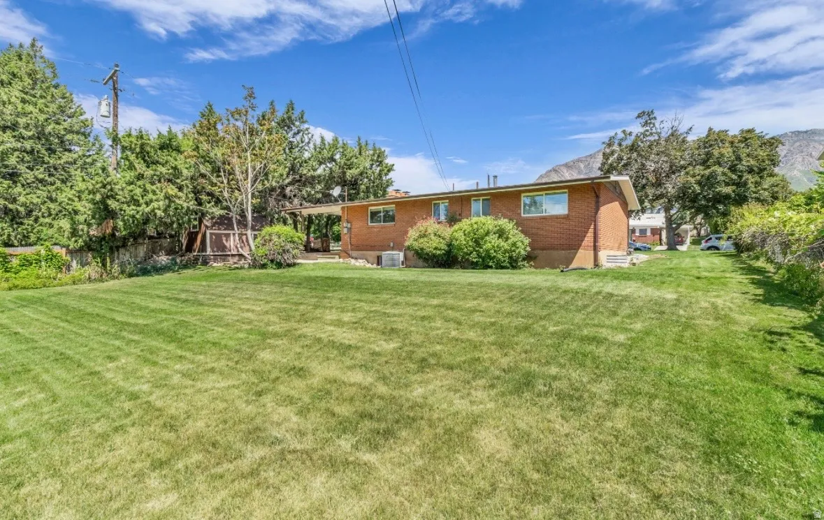 Expansive grassy yard area with mature perimeter trees and a brick-sided residence