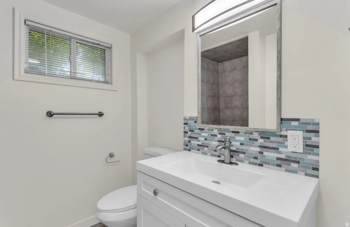 Bathroom featuring a white vanity with integrated sink, brushed nickel faucet, and a multi-tone tile backsplash