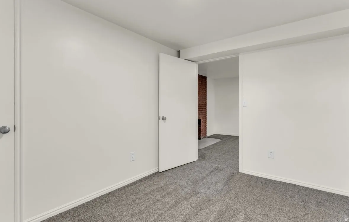 Carpeted room featuring white walls, white trim, and a prominent doorway leading to an additional space with a visible red brick wall