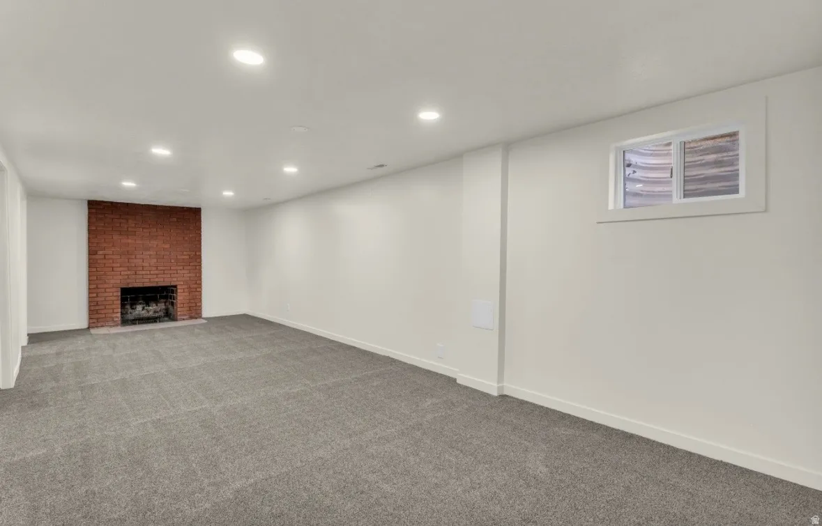 Spacious room featuring a brick fireplace, recessed lighting, and grey carpet flooring