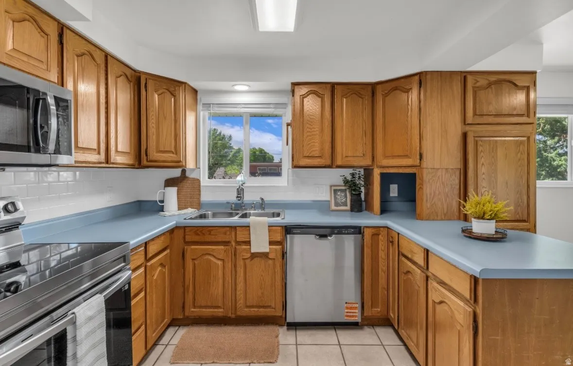 Kitchen featuring abundant natural wood cabinetry, light blue countertops, a double basin stainless steel sink, tile flooring, and a stainless steel dishwasher