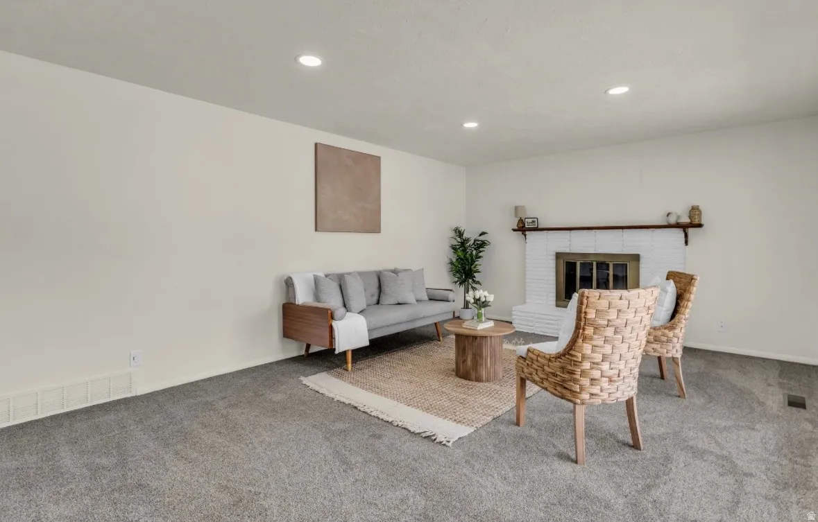 Spacious room featuring neutral carpeting, recessed lighting, and a white brick fireplace with a dark wood mantel