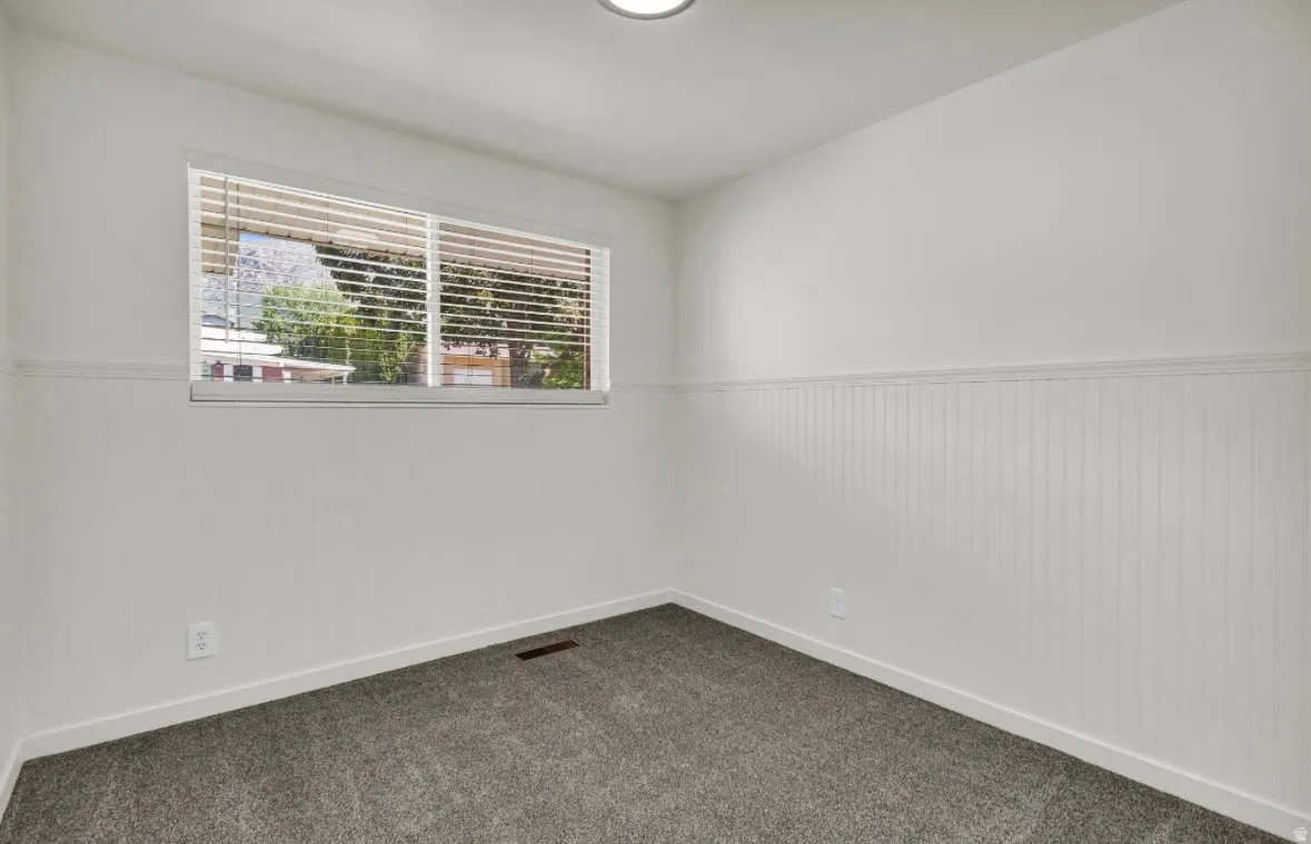 Room featuring beadboard wainscoting, white walls, and a window with horizontal blinds