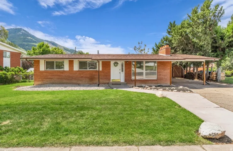 Brick facade home featuring a front yard with green lawn, concrete pathway, attached carport, and a prominent mountain backdrop