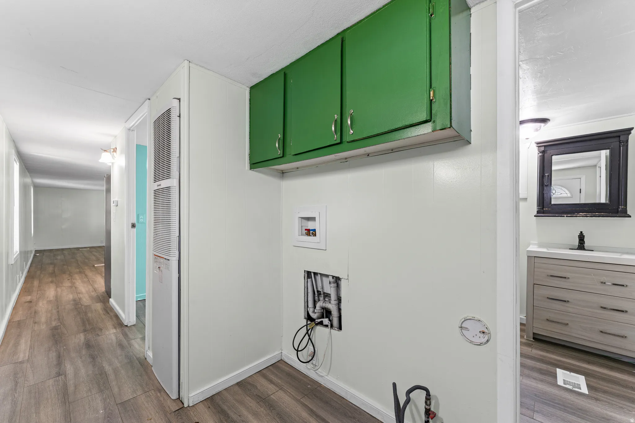 Dedicated laundry area featuring green overhead cabinetry, panel-style walls, and wood-finish flooring