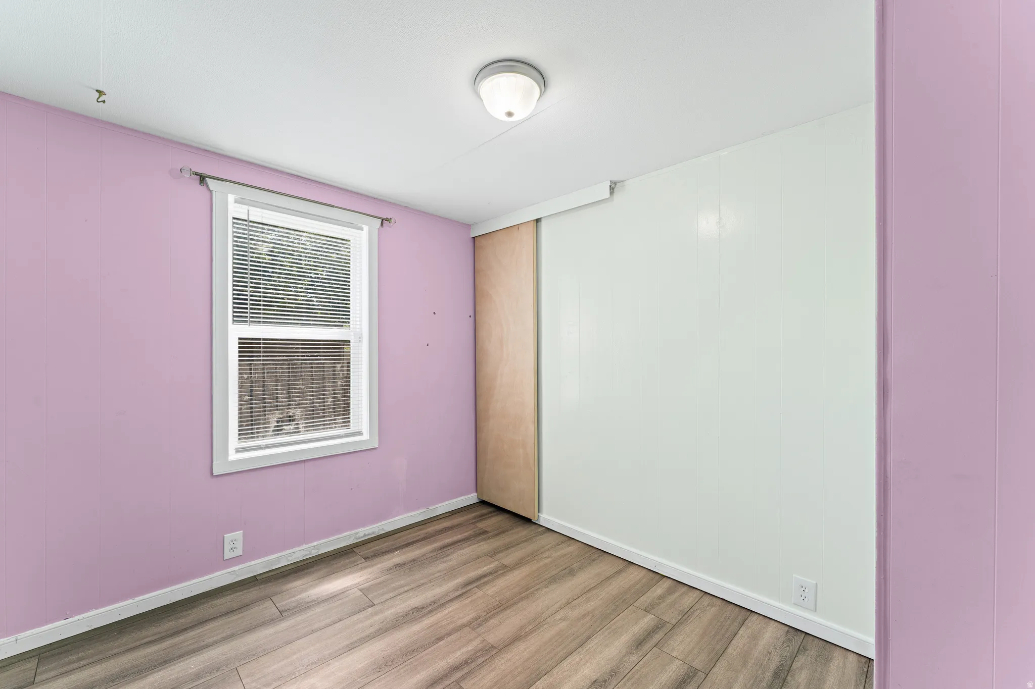 Room featuring wood-finish flooring, a window with horizontal blinds, and a flush mount ceiling light fixture