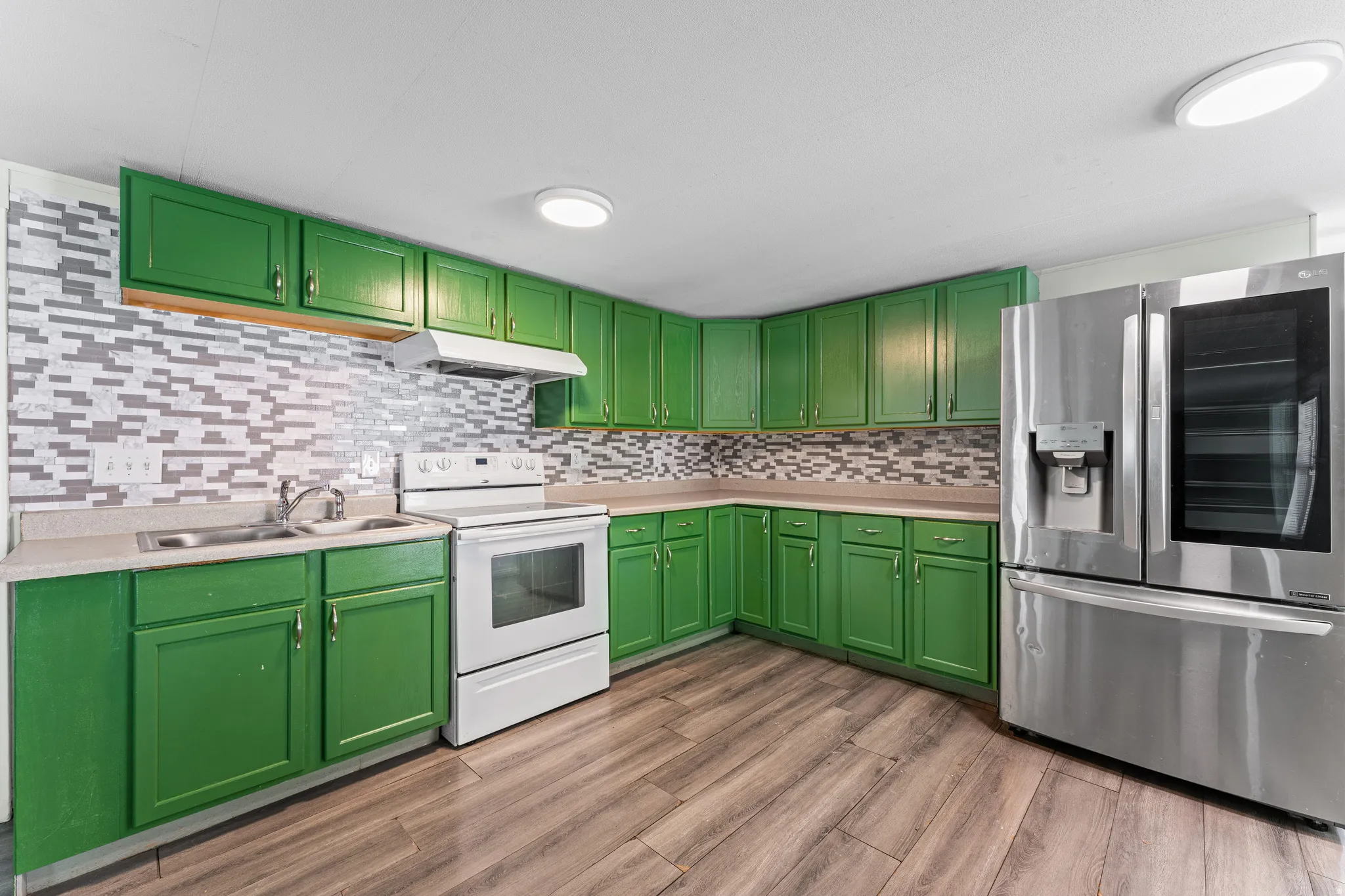 Kitchen featuring green cabinetry, mosaic tile backsplash, wood-finish flooring, a stainless steel refrigerator, and a white electric range with a range hood