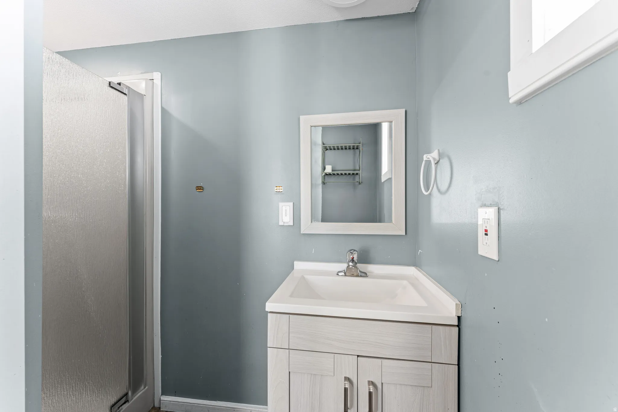 Bathroom featuring a shower enclosure with frosted glass, light blue walls, and a white framed mirror