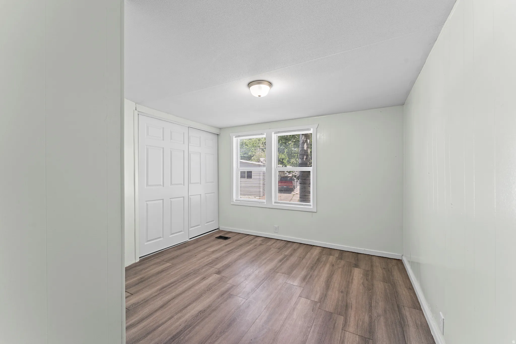 Room featuring wood-finish flooring, light-toned walls, a flush-mount ceiling light, and a double window with white trim