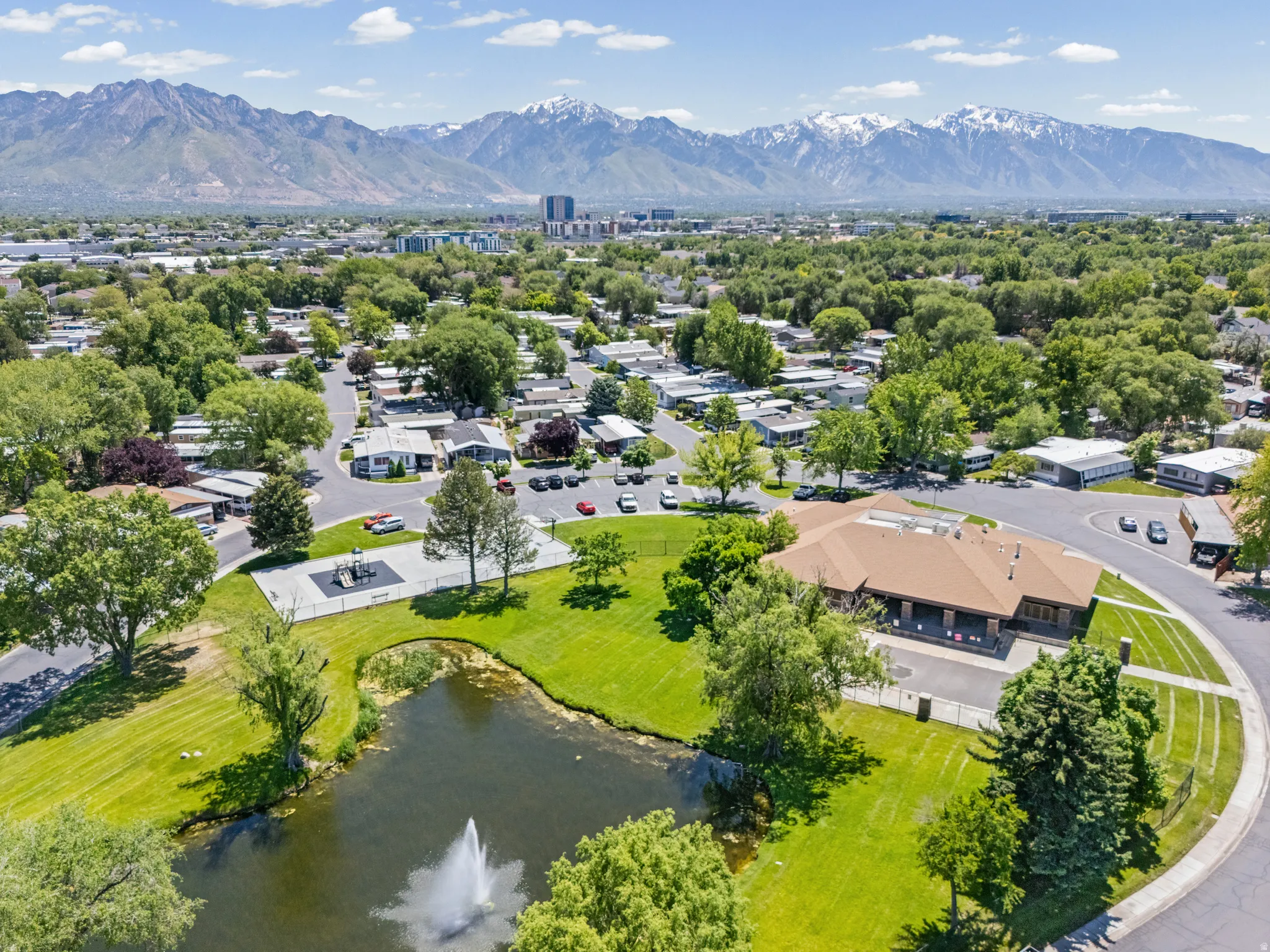 Expansive community grounds featuring a central pond with a fountain, a large green space, and a dedicated play area