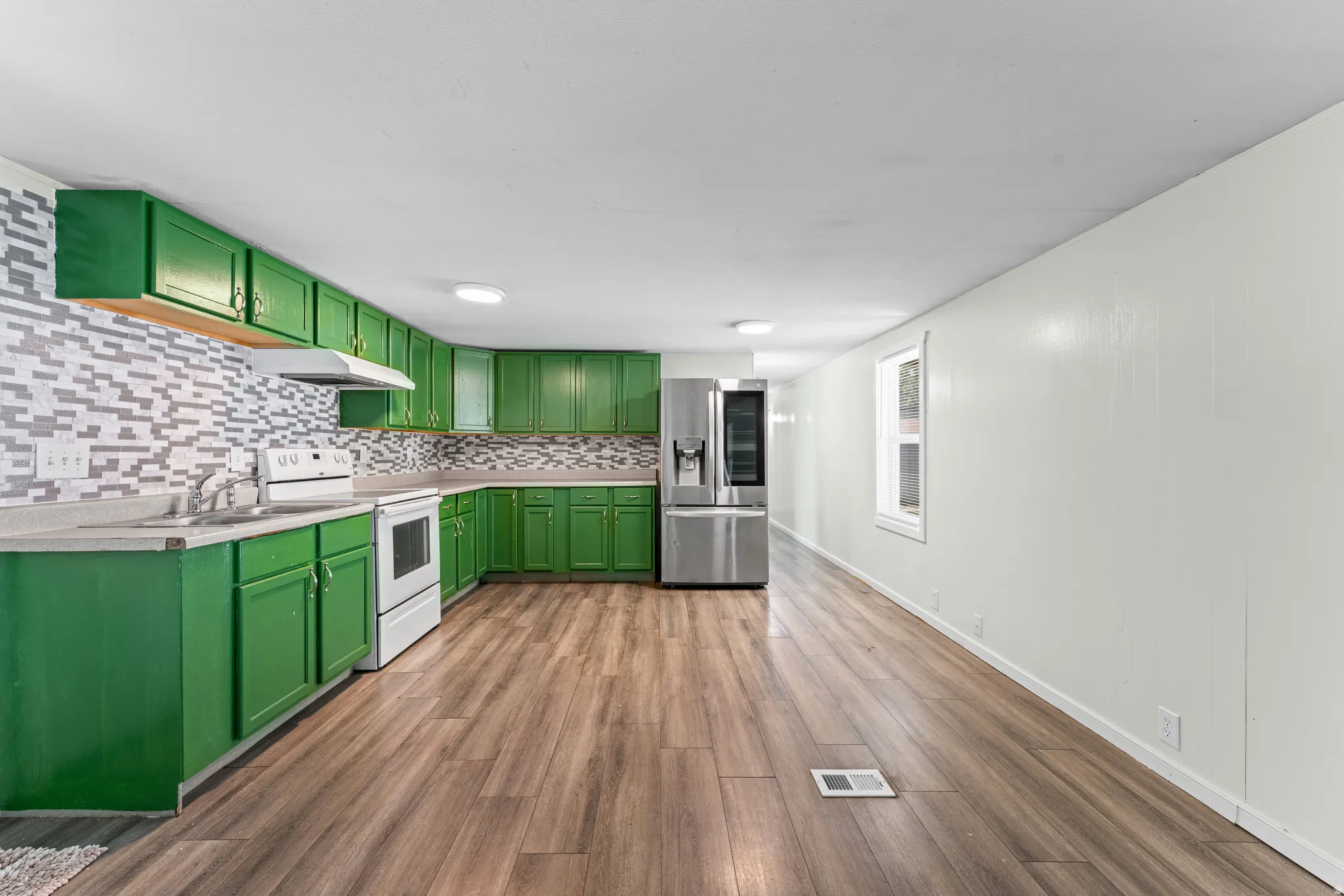 Kitchen featuring green cabinetry, white appliances, a patterned tile backsplash, and wood-finish flooring