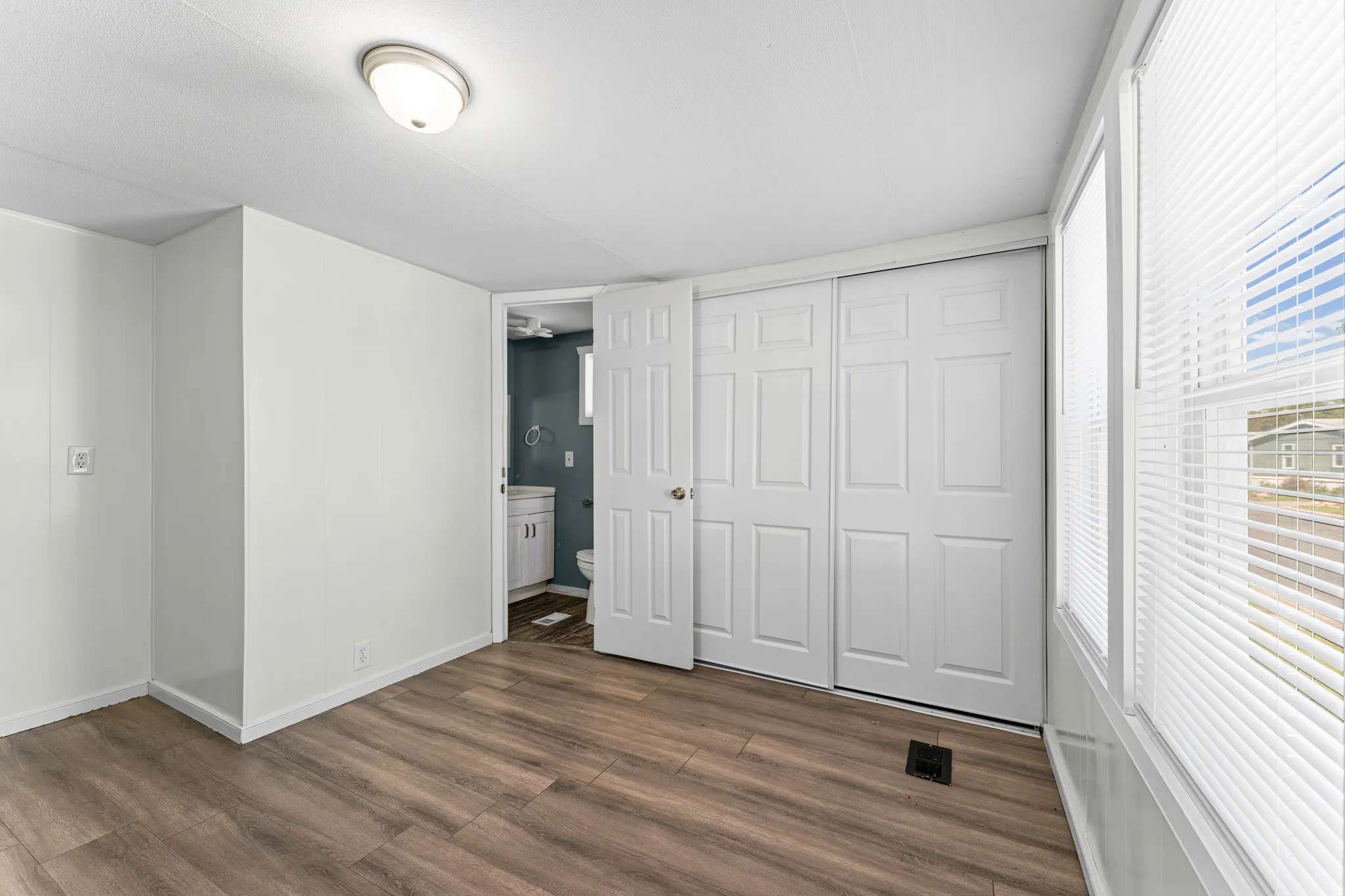 Spacious room featuring wood-finish flooring, white walls, and a ceiling-mounted light fixture
