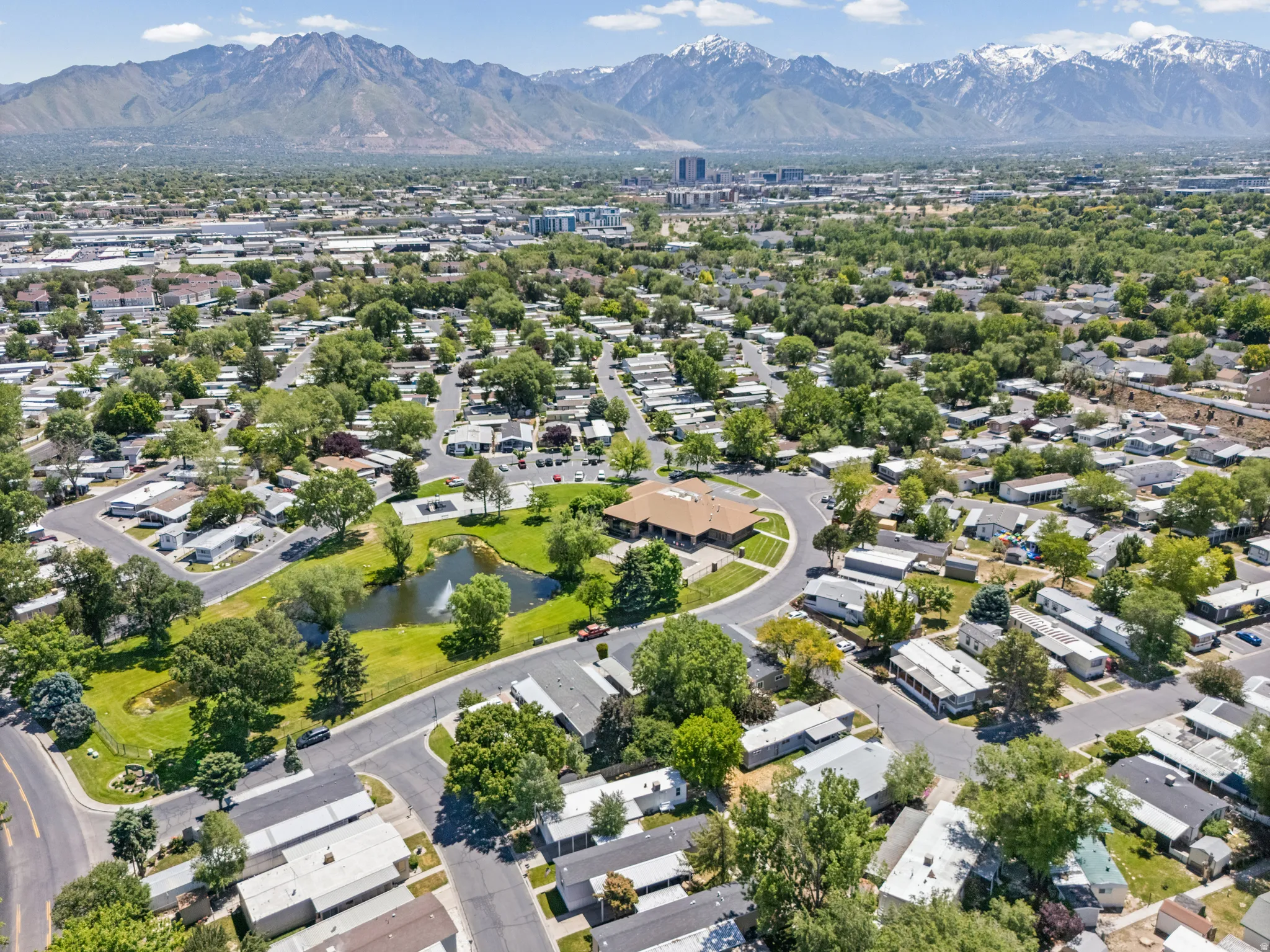 Aerial perspective showcasing a residential community with abundant mature trees and a central pond featuring a fountain