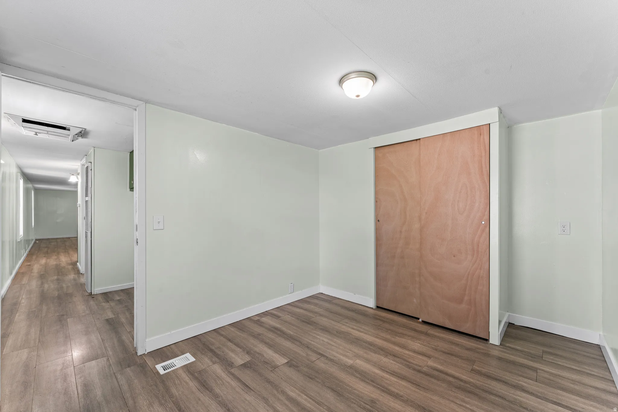 Interior room featuring wood-finish flooring, light-toned wall paint, white baseboards, and a ceiling-mounted light fixture