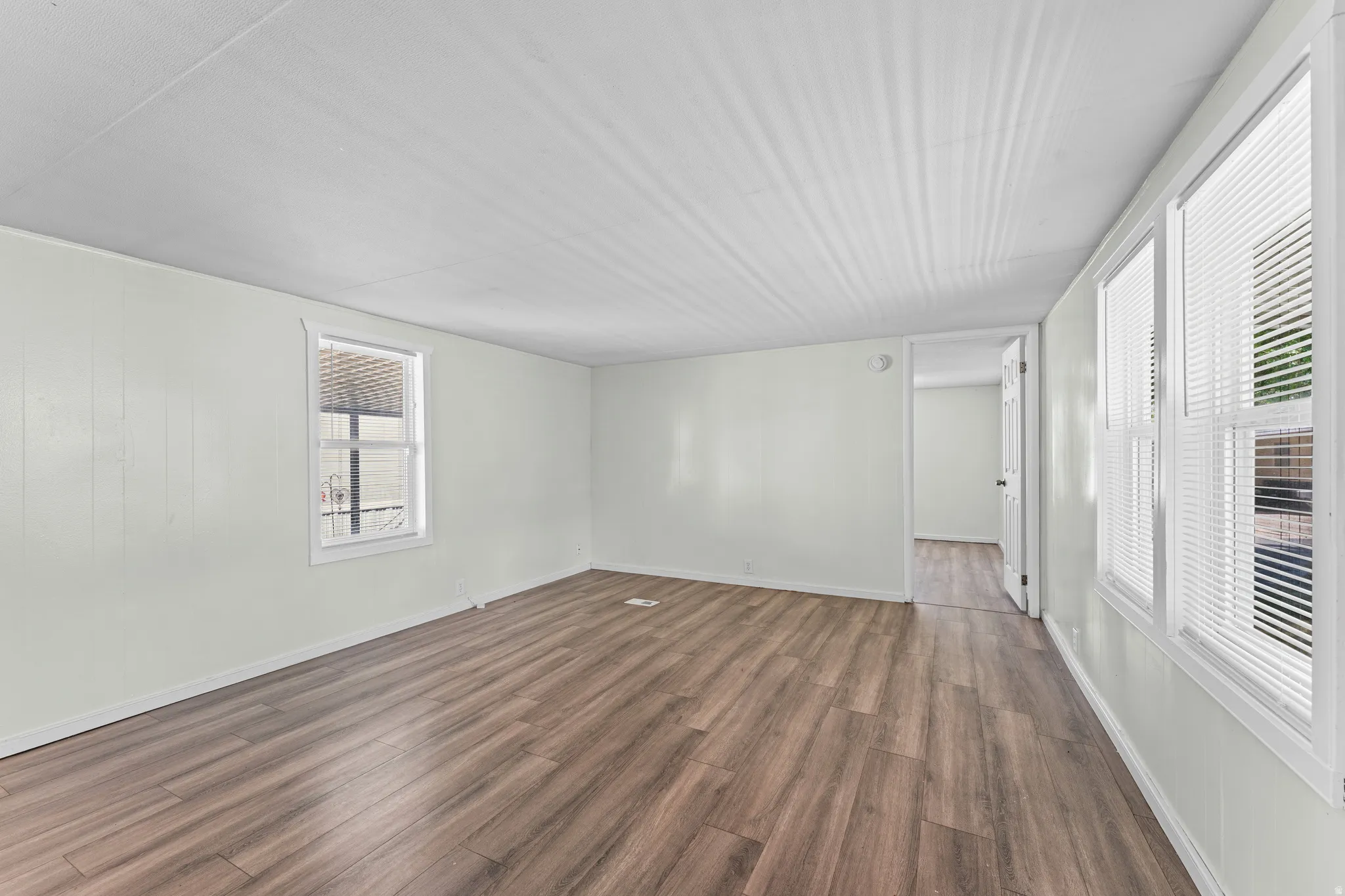 Spacious interior room featuring wood-finish flooring, light-toned walls, and multiple windows with blinds