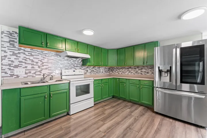 Kitchen featuring green cabinetry, mosaic tile backsplash, wood-finish flooring, a stainless steel refrigerator, and a white electric range with a range hood