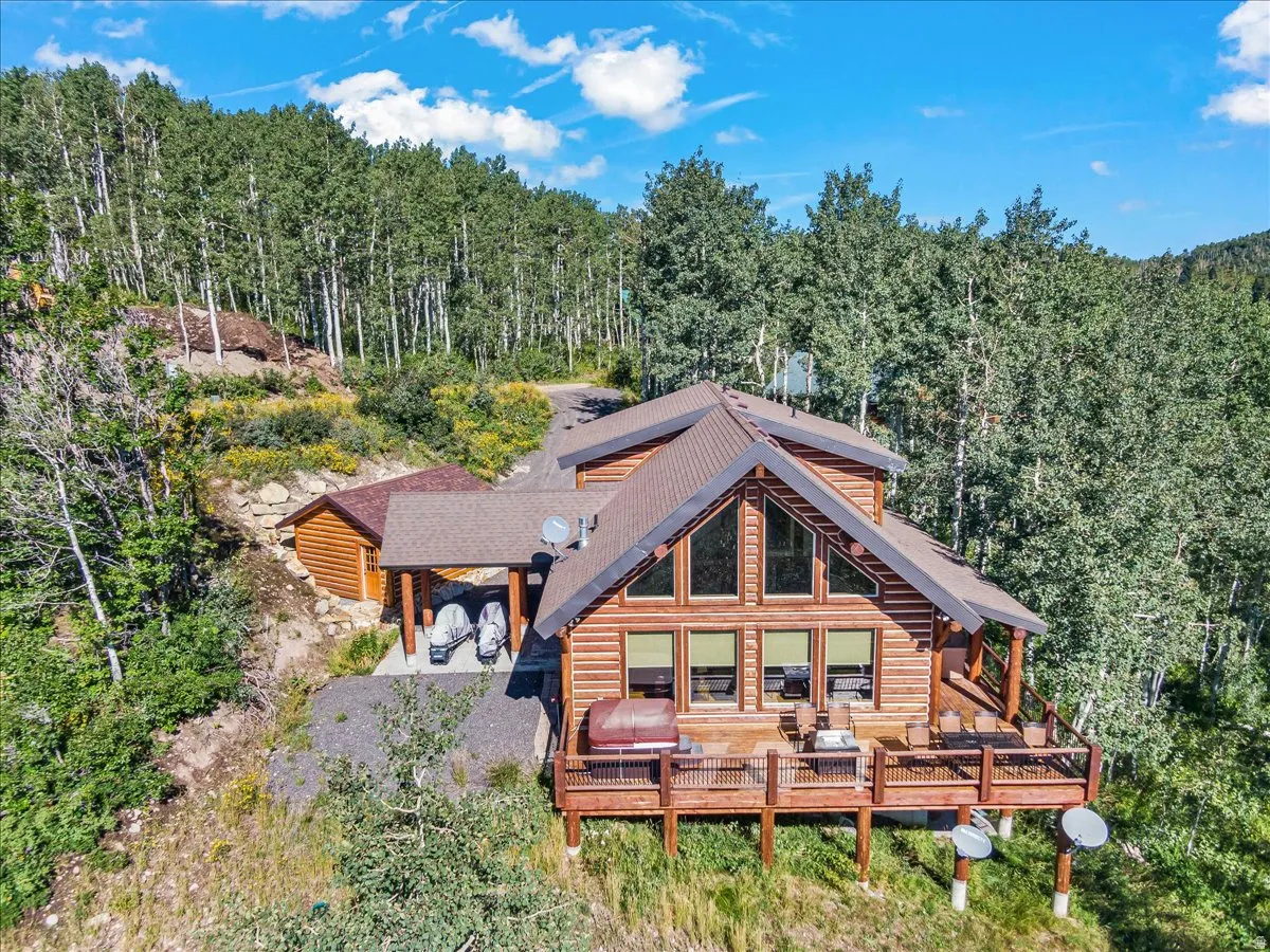 Log cabin exterior featuring a multi-level deck, expansive windows, a covered carport, and a detached outbuilding