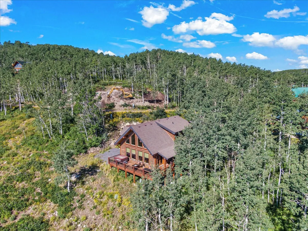 Log cabin residence featuring a multi-level deck, pitched roofline, large window array, and surrounding mature trees