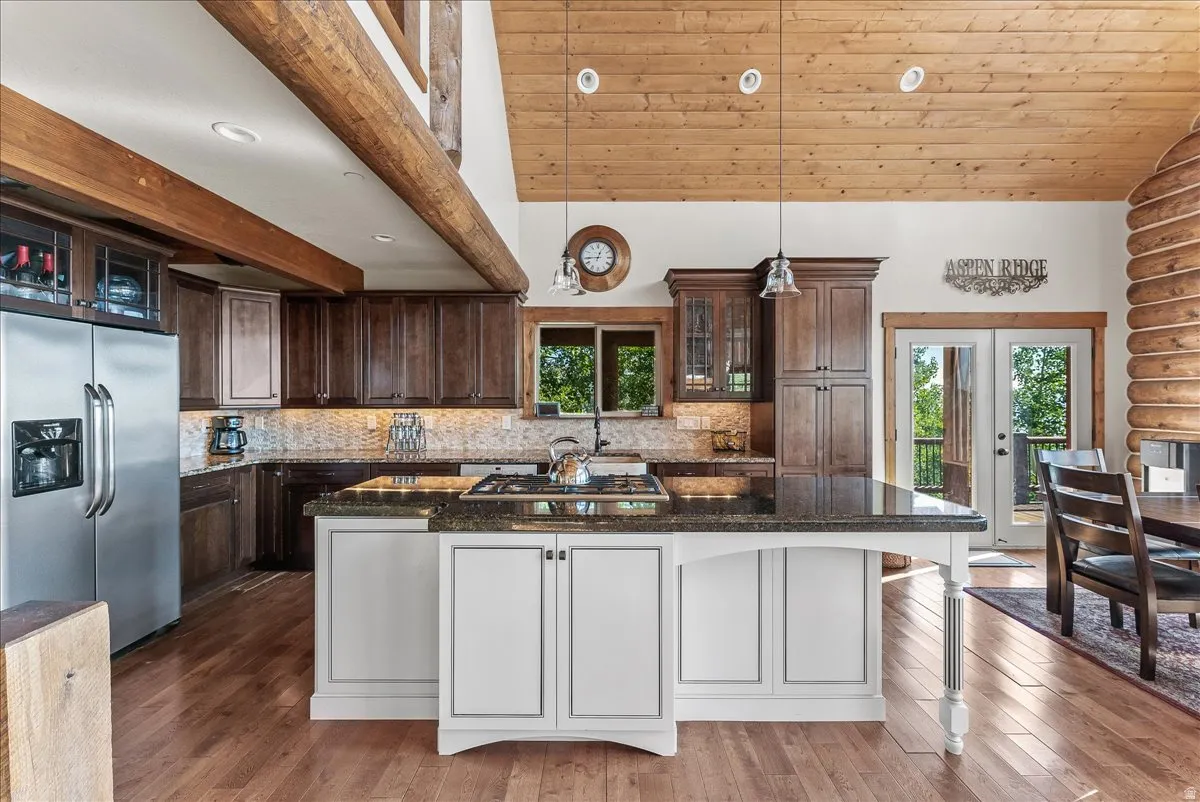 Kitchen featuring wood-finish flooring, dark wood cabinetry, a mosaic tile backsplash, and a central island with a granite-style countertop