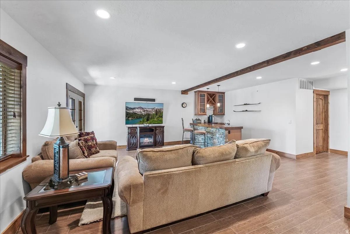Spacious entertainment area featuring wood-finish flooring, recessed lighting, and exposed ceiling beams