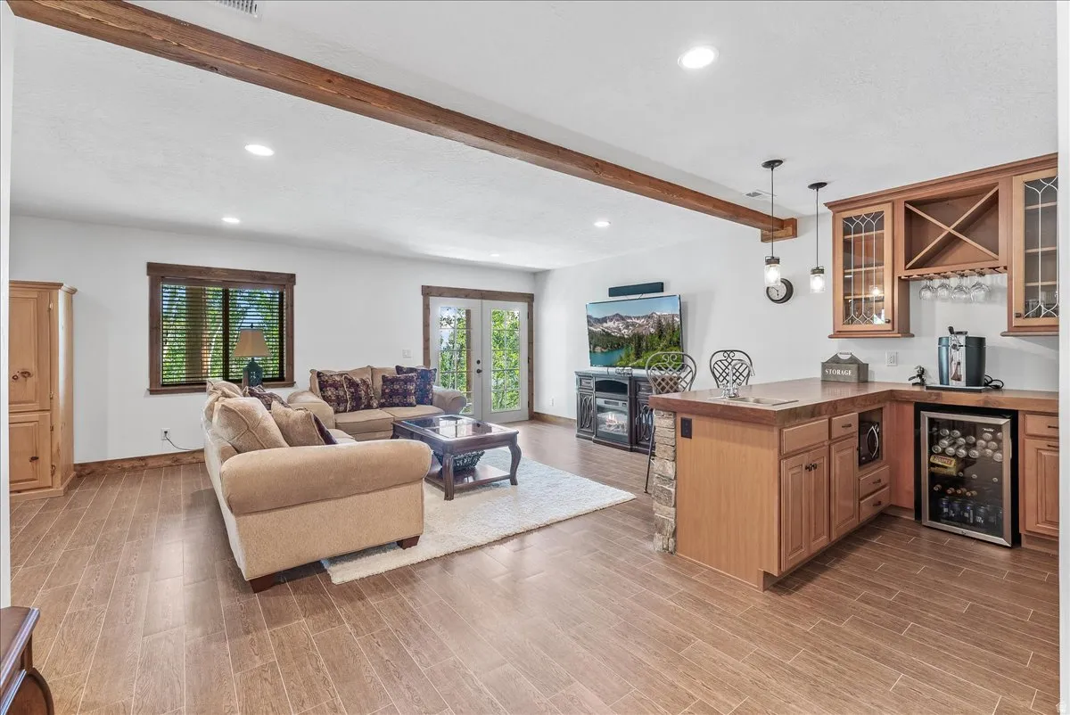 Spacious entertainment area featuring wood-finish flooring, exposed ceiling beam, recessed lighting, and a built-in wet bar with a beverage cooler and wood cabinetry