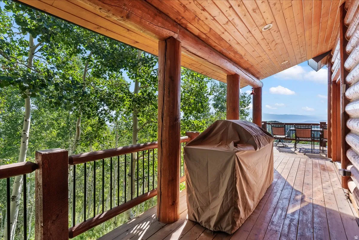 Expansive wood deck featuring a natural wood ceiling, log support beams, wood railing with black spindles, and mountain scenery