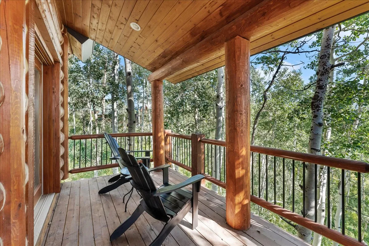 Expansive wood deck with exposed log posts and railings, offering tree canopy surroundings
