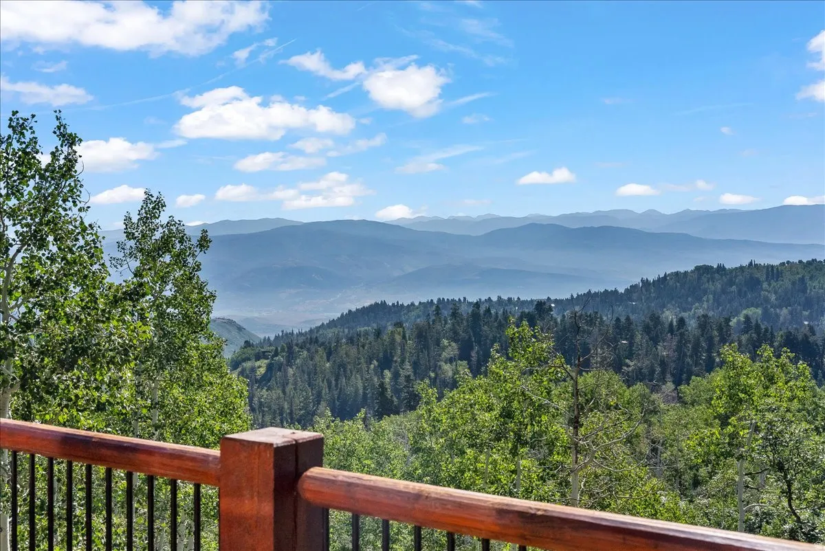 Wood-finish railing with black metal balusters offering expansive mountain and forest scenery