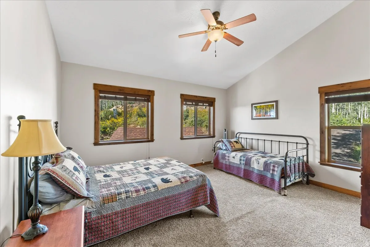 Vaulted ceiling bedroom featuring multiple windows with wood trim, ceiling fan, and carpeted flooring