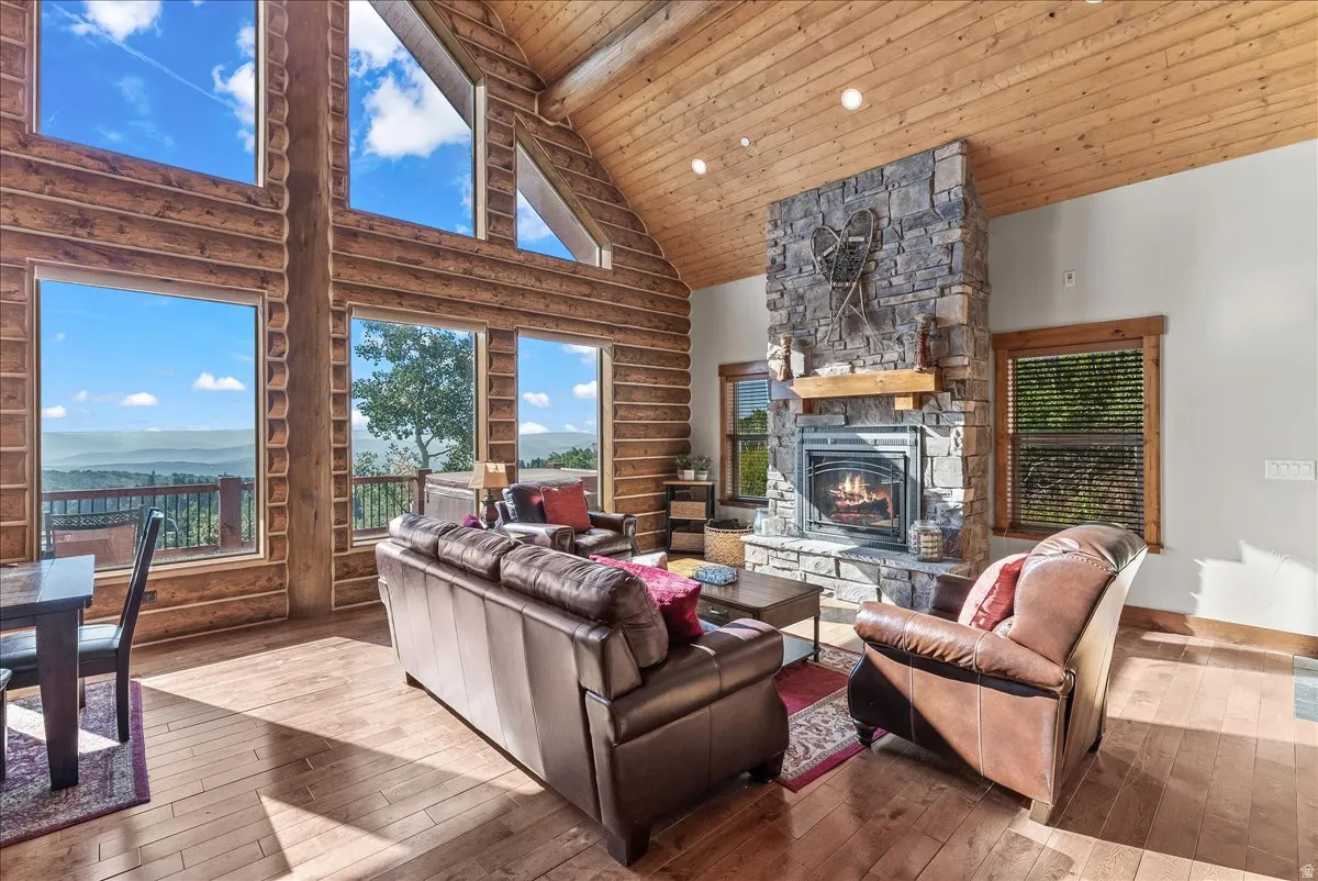 Expansive great room featuring a floor-to-ceiling stone fireplace with a wood mantel, exposed log walls, and wood-finish flooring