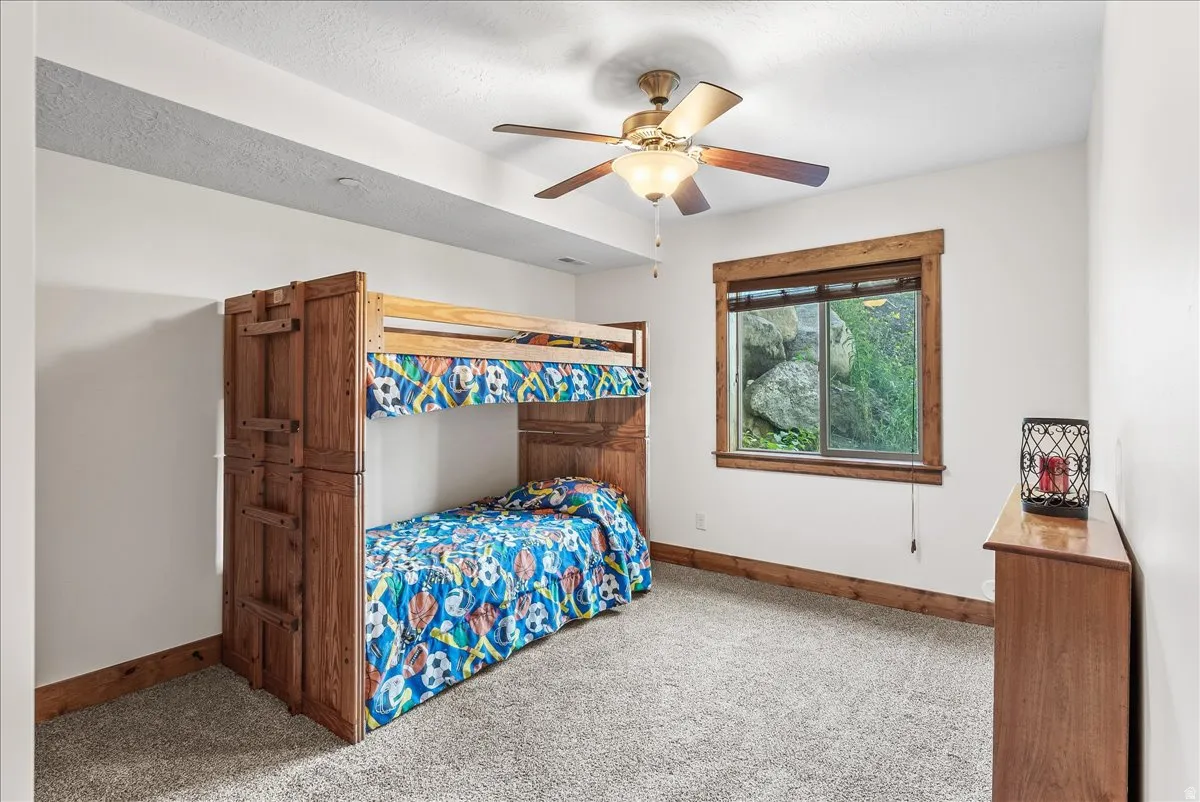 Carpeted room featuring a window with natural wood trim, a ceiling fan, and white painted walls