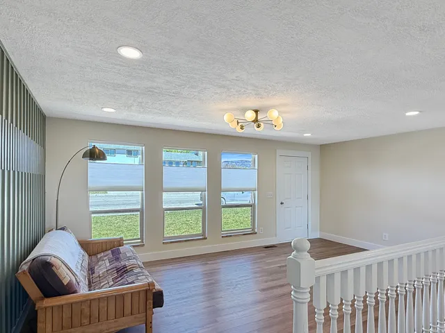 Spacious room featuring wood-finish flooring, a contemporary chandelier, multiple recessed lights, and a corrugated accent wall