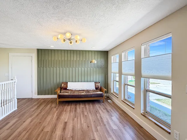 Spacious room featuring wood-finish flooring, a decorative accent wall, and multiple windows with custom blinds